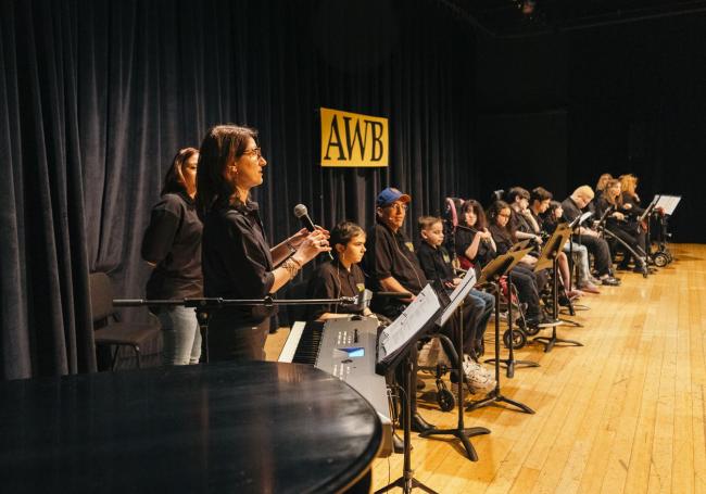 Young people with diverse abilities sit behind music stands on a stage